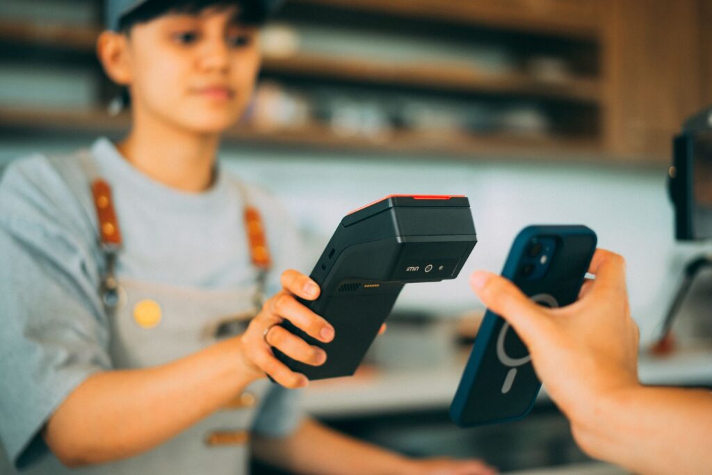 Cafe employee holding a portable card reader while a customer pays with tap-to-pay on a phone