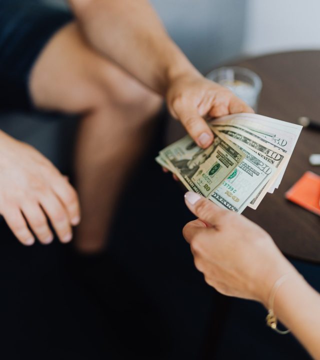 Close-up of hands exchanging US dollar bills, symbolizing a financial transaction or payment.